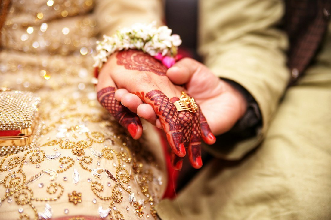 Hands with henna and gold rings resting on a golden lehenga